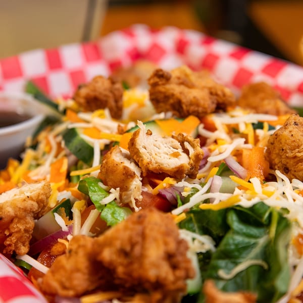Crispy fried chicken pieces, shredded cheese, and vegetables on a bed of lettuce in a red checkered basket.