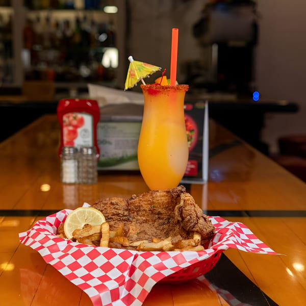 Fried fish and french fries in a basket with a lemon slice, next to a daiquiri.