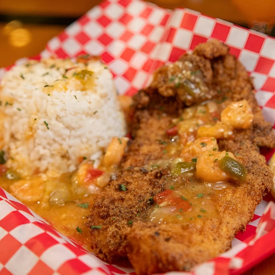 Fried fish with shrimp and vegetable sauce, served with white rice in a red and white checkered basket.
