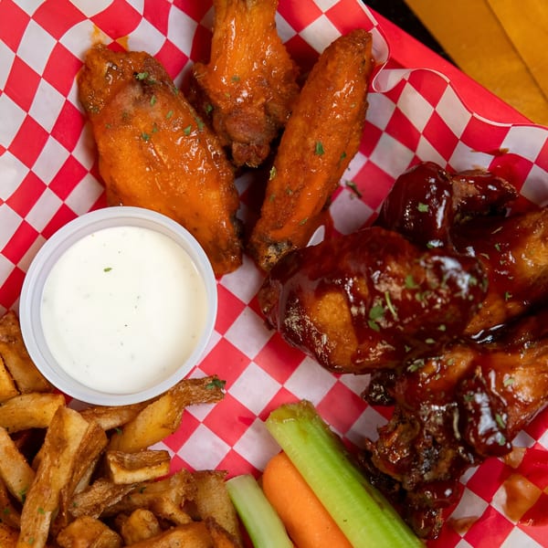 A basket of Sooner Daiquiri chicken wings, fries, ranch, celery, and carrots.
