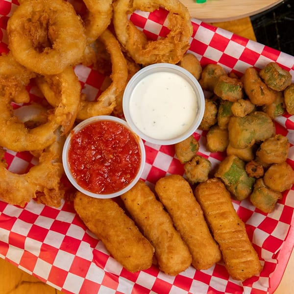 A basket of fried onion rings, mozzarella sticks, and fried okra with marinara and ranch.