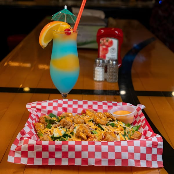 Sooner Daiquiri's fried shrimp salad with dressing, and a blue and yellow daiquiri on a wooden table.