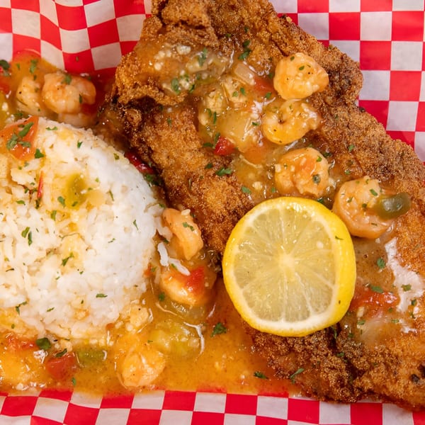 Fried fish fillet with shrimp and rice, garnished with a lemon slice, on a red and white checkered paper.