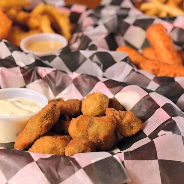 Fried mushrooms and dipping sauce in a checkered paper-lined basket, with other fried foods in the background.