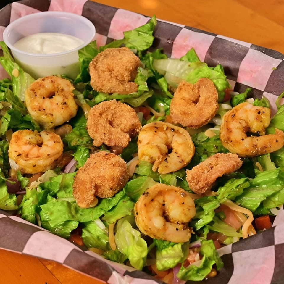 A fresh green salad with grilled and fried shrimp, served with a side of ranch dressing.