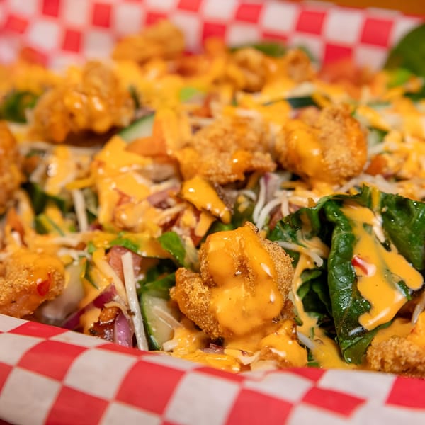 Crispy fried shrimp salad with mixed greens, cheese, and orange dressing in a red checkered basket.